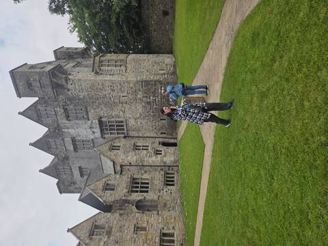 Visitors walking on the lawn outside a grey-stone castle with tall gables