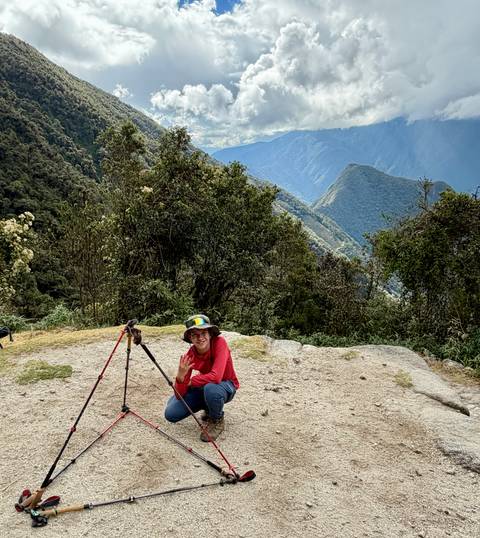 Trekker crouching with trekking poles on a viewpoint overlooking lush mountain ridges