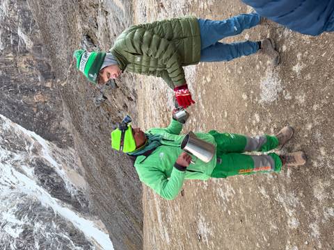 Guide serving a hot drink to a trekker on a frosty mountain morning