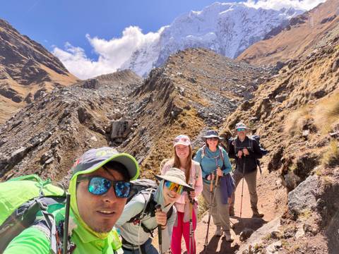Group selfie on a rocky alpine pass with snow-covered peak towering behind