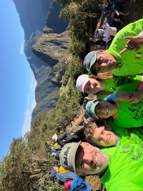 Happy trekkers wearing matching shirts with Machu Picchu ruins and Huayna Picchu behind