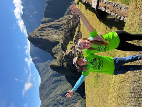 Two young trekkers celebrating with Machu Picchu’s stone terraces in bright sunlight behind them