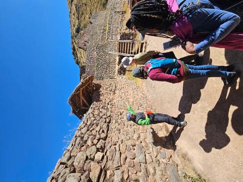 A guide gestures toward stone terraces at an Inca archaeological site under a deep blue sky.