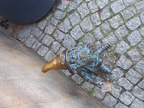 Small bronze gnome statue wearing a pointed hat on a cobblestone pavement.