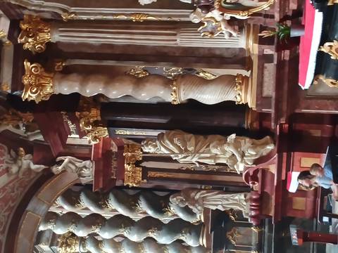 Opulent baroque church interior with twisted marble columns, gilded statues and a richly decorated altar.