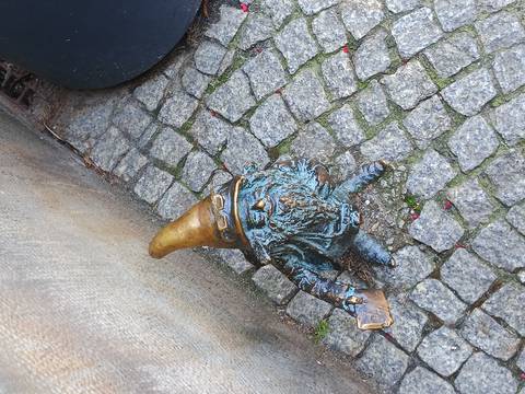 Close-up of a bronze dwarf statue with a golden hat standing on cobblestone pavement.