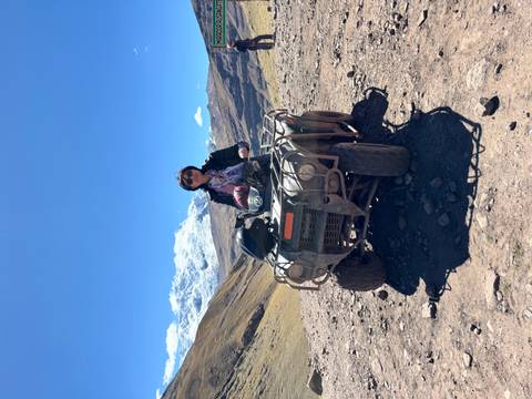 Person riding an ATV on a rugged mountain trail with snow-capped Andes peaks in the background.