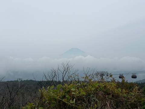 Distant peak of Mount Fuji barely visible above heavy clouds with cable-car towers in foreground.