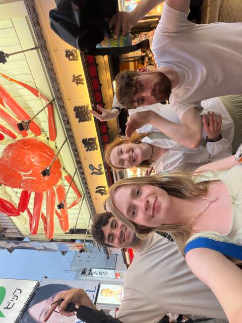 Travelers pose for a selfie beneath the giant mechanical crab sign in Osaka’s Dotonbori district.