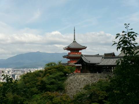 Red pagoda of Kiyomizu-dera overlooks Kyoto city with mountains and trees framing the view.