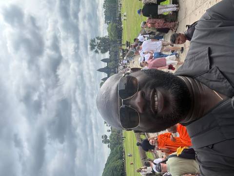 Selfie with crowds approaching the towers of Angkor Wat beneath a dramatic cloudy sky.