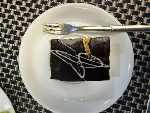 Close-up of a small chocolate pastry square with decorative white icing next to a fork.