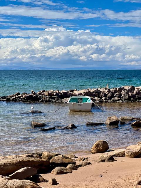 Small white boat moored to rocks on the clear blue waters of Lake Titicaca
