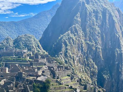 Steep green cliff of Huayna Picchu towers above the stone structures of Machu Picchu
