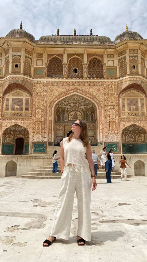 A traveler wearing sunglasses stands before the intricately painted Ganesh Pol gateway at Amber Fort in Jaipur.
