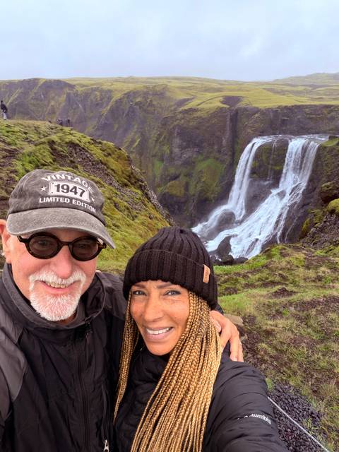 Happy couple posing in front of a dramatic mossy cliff and ribbon waterfall
