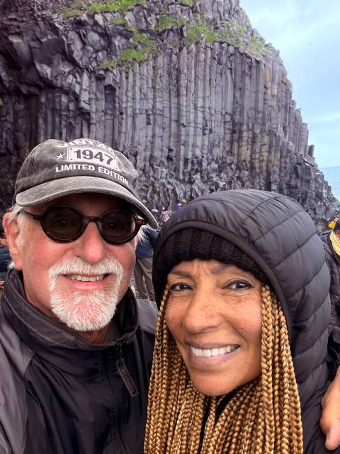Close selfie of couple with dramatic columnar basalt cliffs on an Icelandic beach behind them