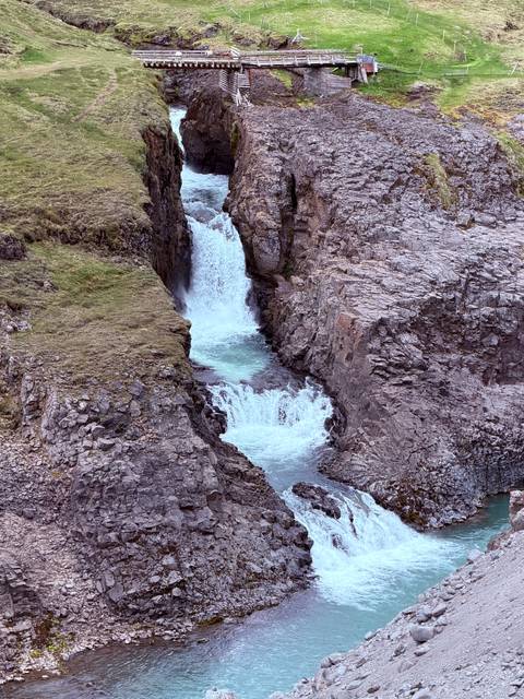 Narrow twin waterfalls dropping into a rocky gorge surrounded by tundra vegetation
