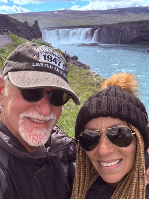 Partial selfie of a couple with a bright blue river and grassy bank behind