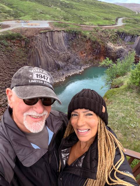 Couple smiling with a turquoise pool in a columnar basalt canyon below them