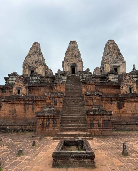 Ancient brick temple with three towers and steep central staircase under grey sky