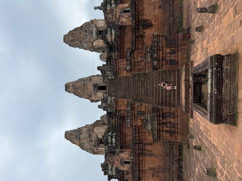 Wide view of temple staircase with two visitors seated halfway up under cloudy skies