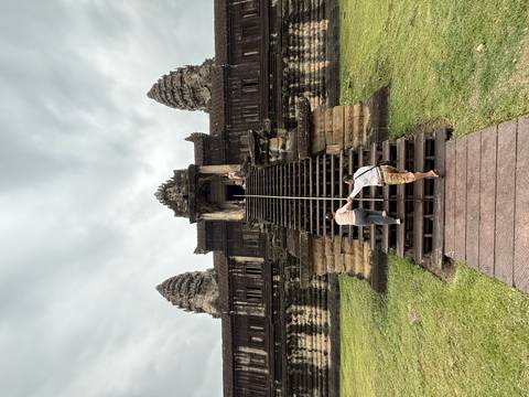 Elderly visitors climbing steep wooden steps with handrail toward an Angkor Wat doorway