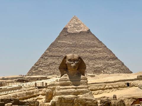 The Great Sphinx sits before the towering Great Pyramid on a bright desert day.