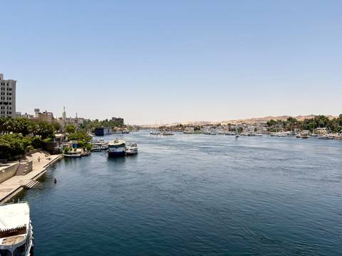 Boats line the broad Nile River as a city stretches along both banks on a sunny day.