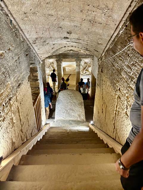 Visitors descend stone steps into an ancient chamber lined with carved reliefs.