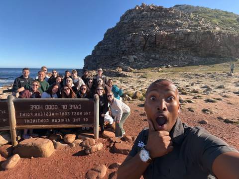 Tour group taking selfie at Cape of Good Hope sign with rocky coast backdrop