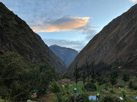 V-shaped green valley at dawn with snow-capped Andean peaks under colorful clouds.
