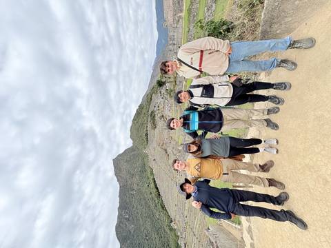 Six hikers posing together in front of stone terraces of Machu Picchu.