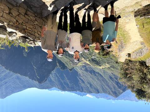 Group of six smiling trekkers at viewpoint above Machu Picchu ruins and mountains.
