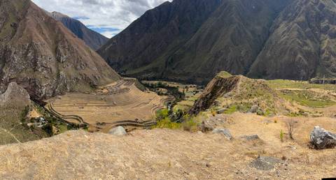 Wide pano of Sacred Valley agricultural terraces and arid mountains under partly cloudy sky.