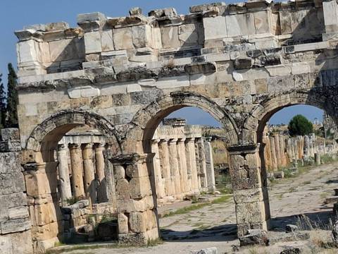 Angled view of arched Roman ruins and colonnaded street under clear blue sky.
