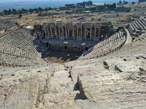 Panoramic view down into a well-preserved Roman amphitheater with tiered stone seating.