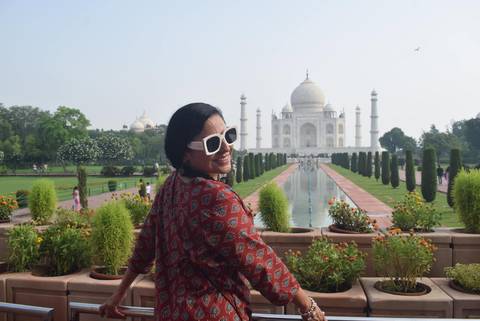 Woman in patterned dress looks back smiling with the reflecting pool leading to the Taj Mahal.