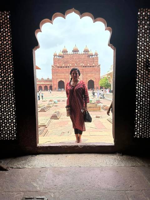Traveller framed in a stone doorway looking onto the vast red sandstone courtyard of a Mughal monument.