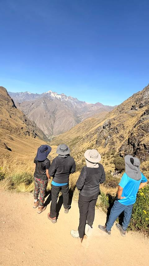 Three hikers with wide-brim hats admiring a vast Andean mountain valley on the Inca Trail.