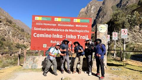 Trekking group posing at welcome sign for the Camino Inka-Inka Trail with mountains in background.