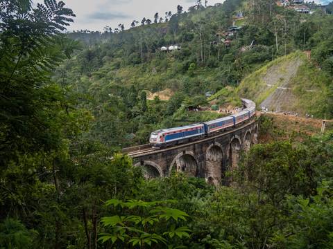 Blue and red train crosses the historic Nine Arches Bridge amid lush green jungle near Ella.