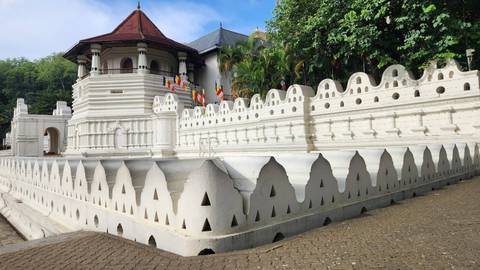 White crenellated walls and a red-roofed octagonal tower of the Temple of the Tooth in Kandy.