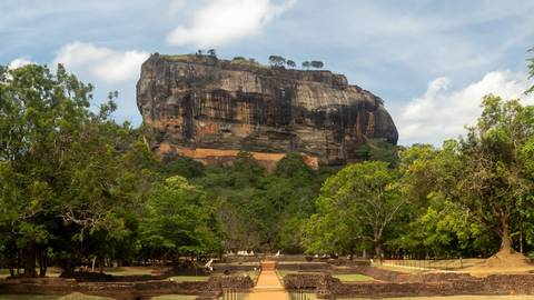 The majestic Sigiriya rock fortress rises above lush jungle and ancient brick foundations.