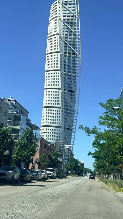 The futuristic Turning Torso skyscraper twisting into a clear blue Swedish sky with nearby modern apartments.