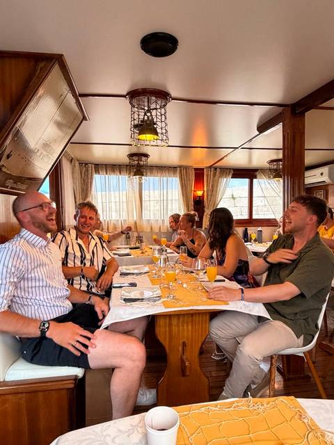 Lively group enjoying drinks and laughter inside a cozy boat dining cabin.
