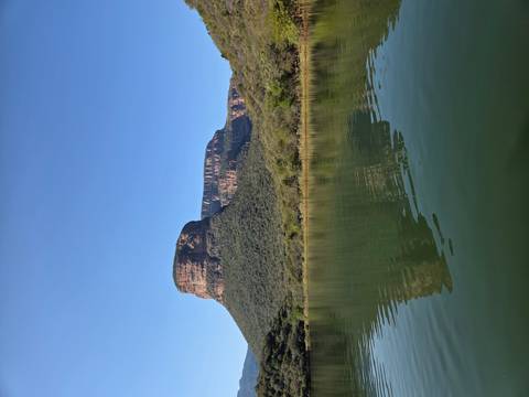 Steep rock mesa reflecting in calm green water beneath a clear blue sky at Blyde River Canyon.