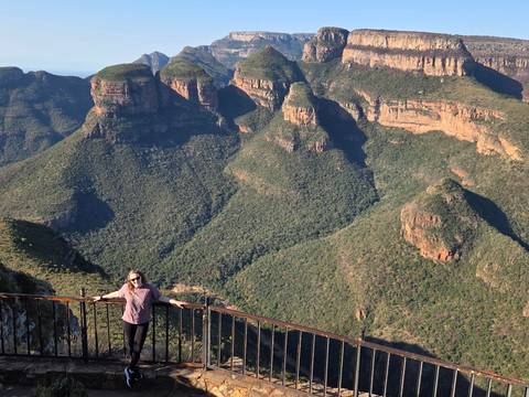 Woman leaning on a viewing railing high above the dramatic green peaks of Blyde River Canyon.