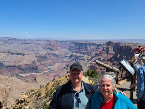 Travellers smile at a panoramic lookout over the layered cliffs and winding Colorado River of the Grand Canyon.