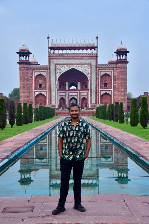 Traveller stands by the long reflecting pool facing the ornate main gate of the Taj Mahal complex.